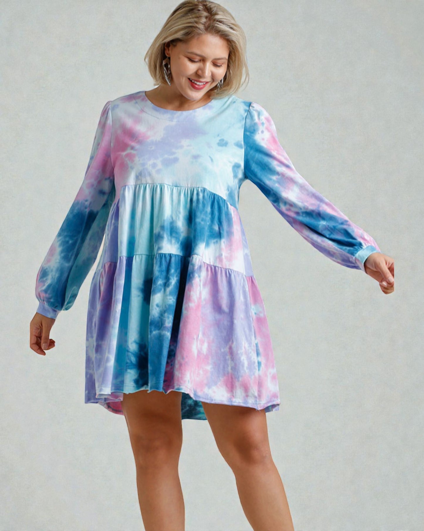 Woman wearing a tie-dye dress with long sleeves on a plain background