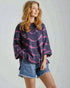 Woman wearing a dark sweater with pink patterns and denim shorts on a light background