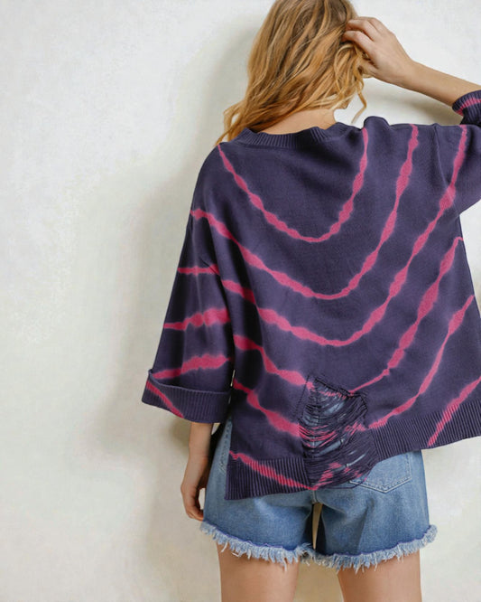 Person wearing a purple and pink tie-dye cardigan with denim shorts on a plain background