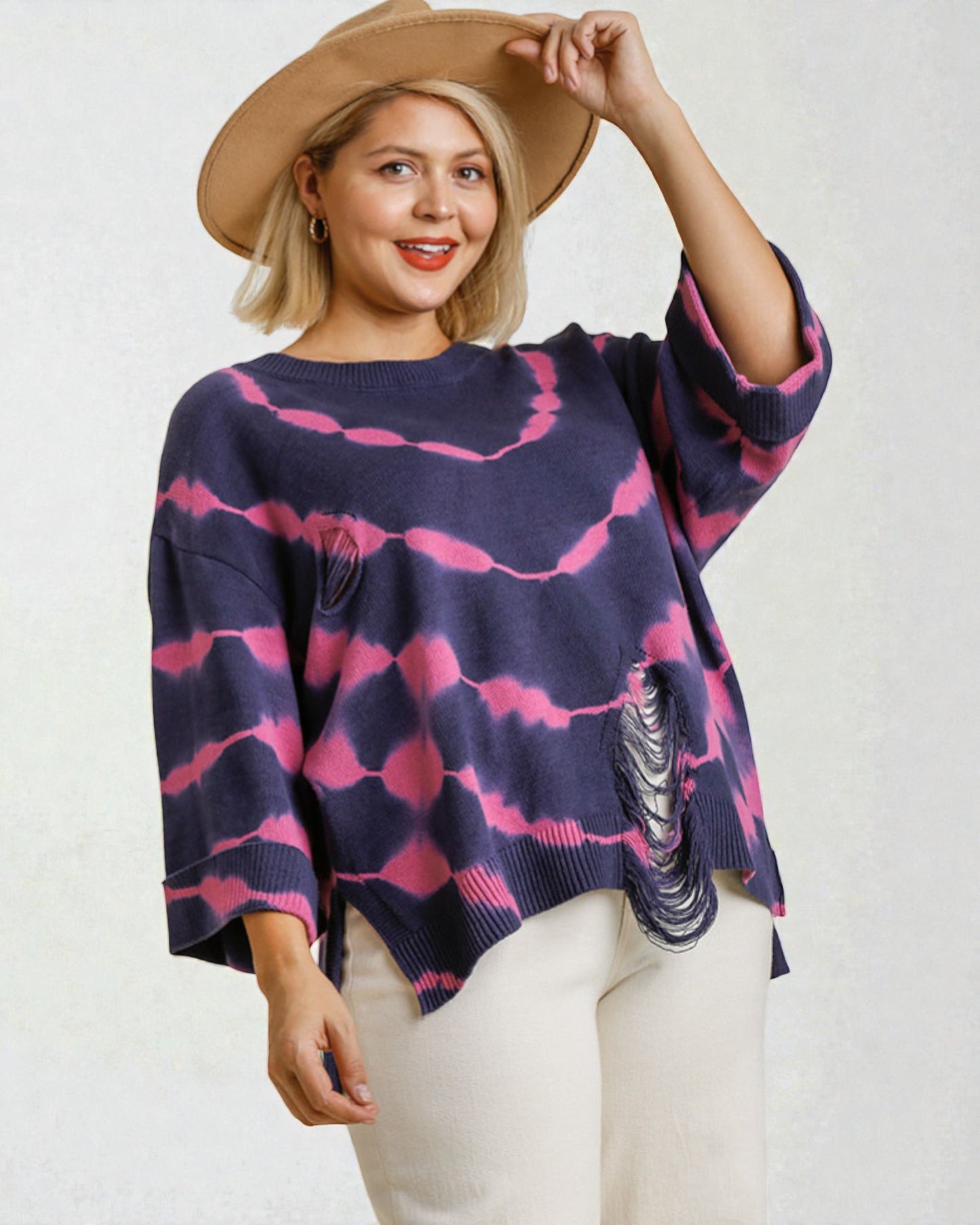 Woman wearing a navy and pink patterned sweater with a beige hat on a white background