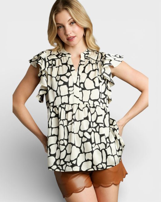 Woman wearing a patterned blouse with ruffled sleeves on a plain background