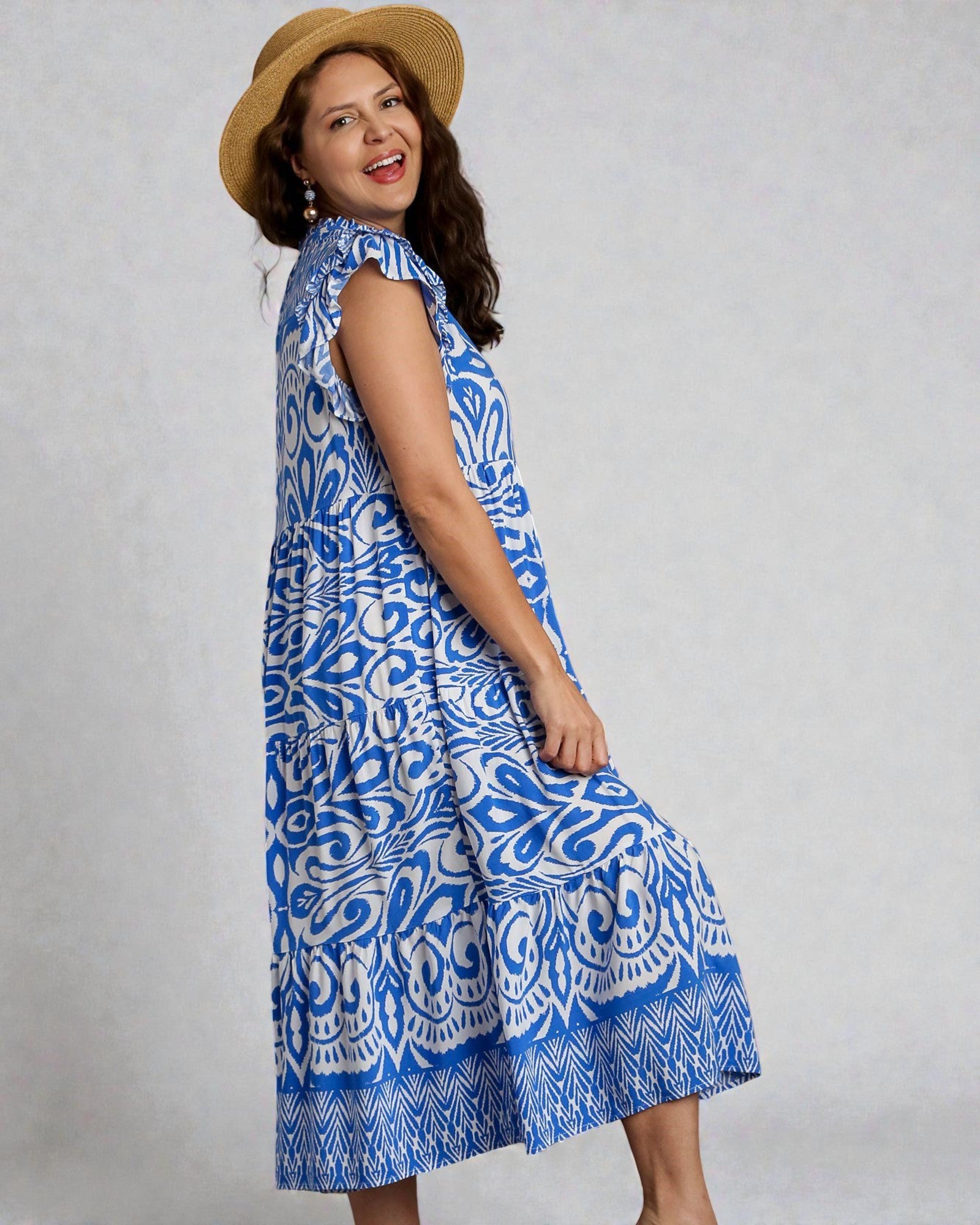 Woman wearing a blue patterned dress and straw hat against a gray background