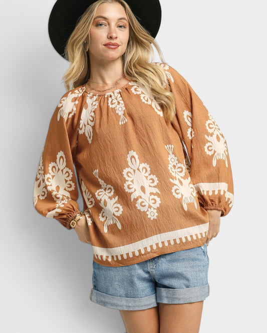Woman wearing a brown blouse with white patterns and denim shorts on a plain background