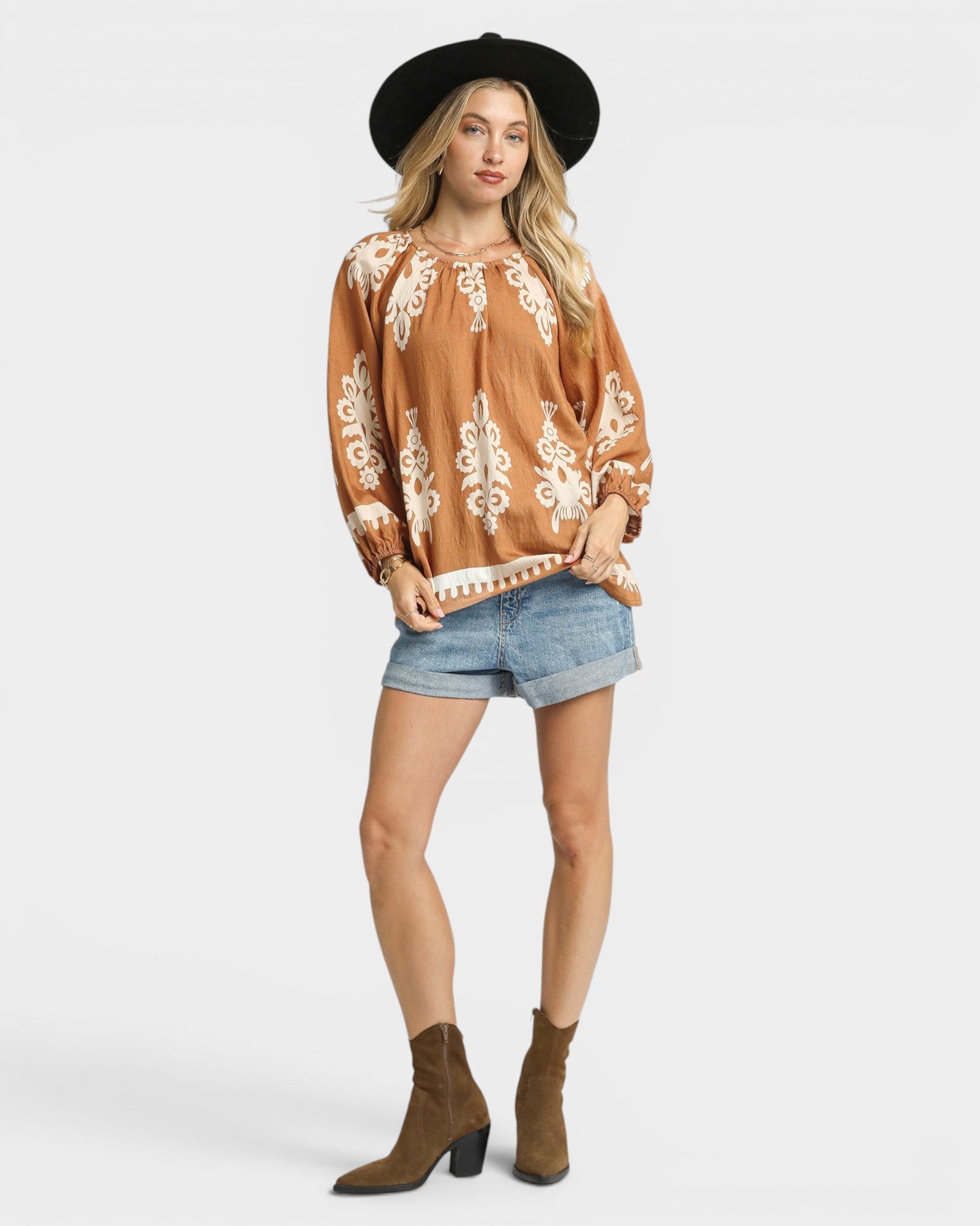 Woman wearing a patterned blouse, denim shorts, and brown boots on a white background