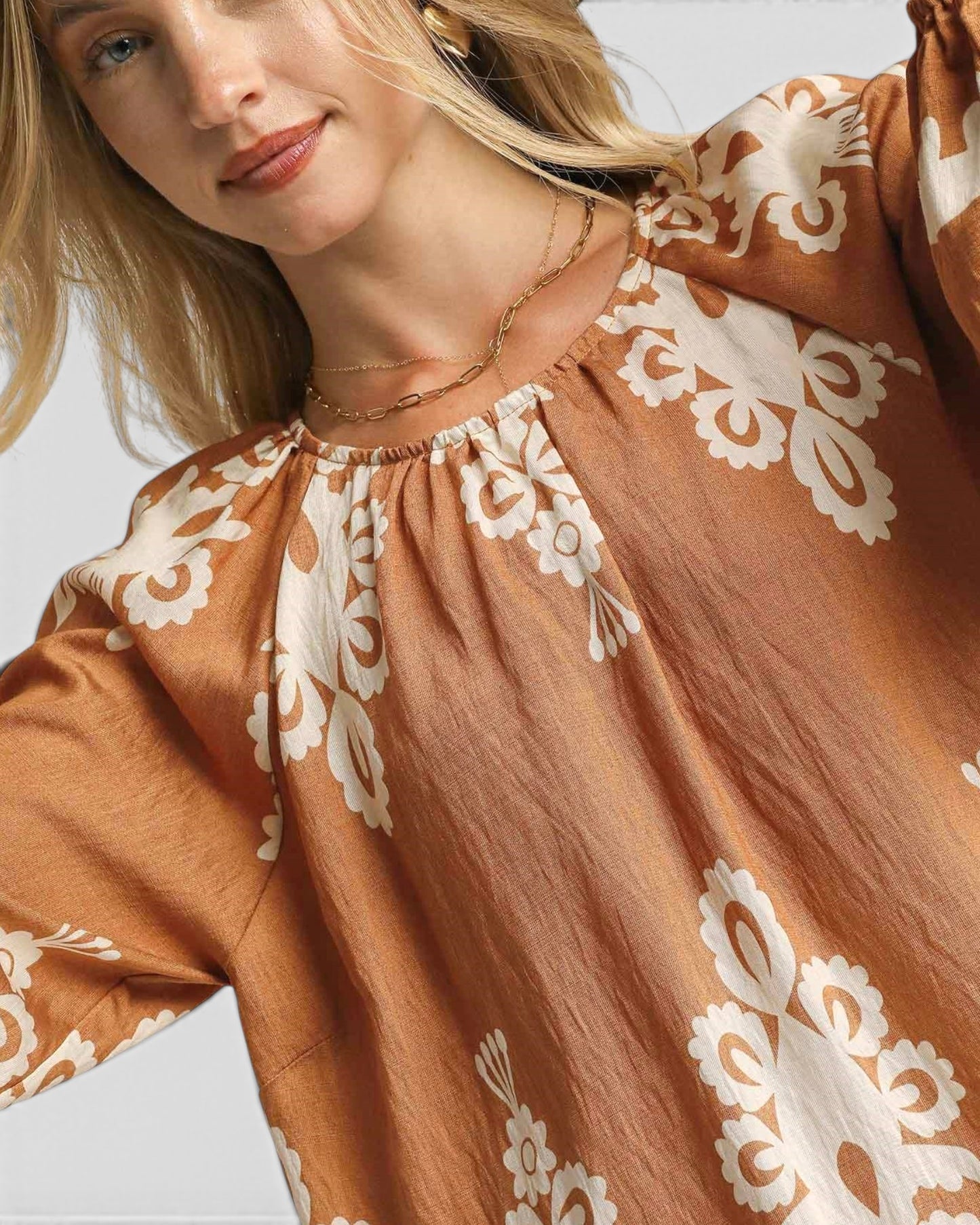 Woman wearing a brown blouse with white lace patterns on a neutral background
