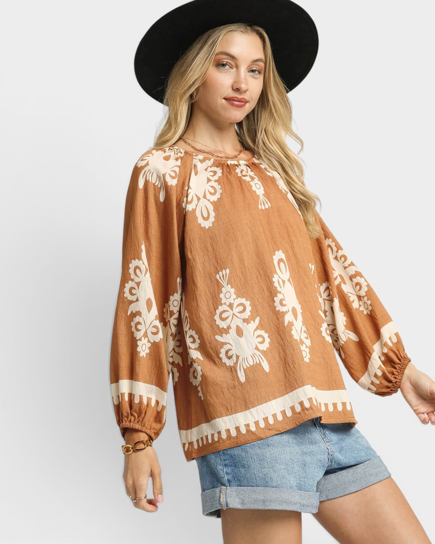 Woman wearing a brown blouse with white patterns and denim shorts on a white background