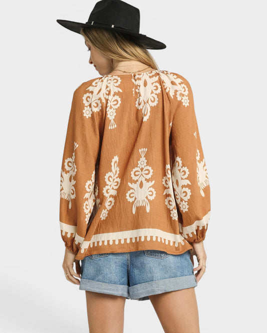 Woman wearing a brown patterned top and denim shorts with a black hat on a white background