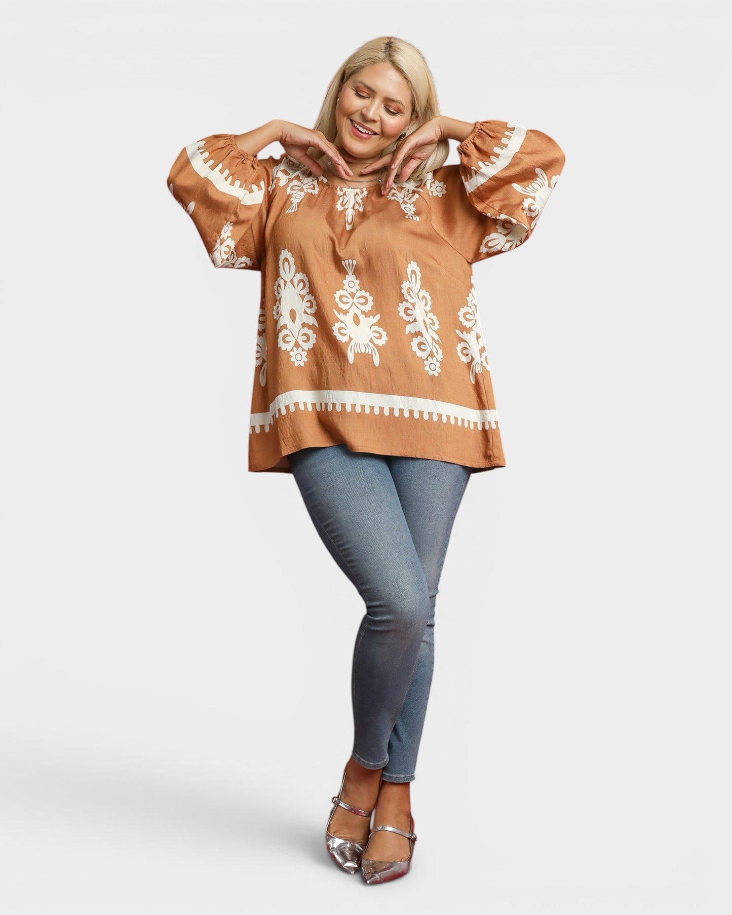 Woman wearing a brown blouse with white patterns and blue jeans on a white background