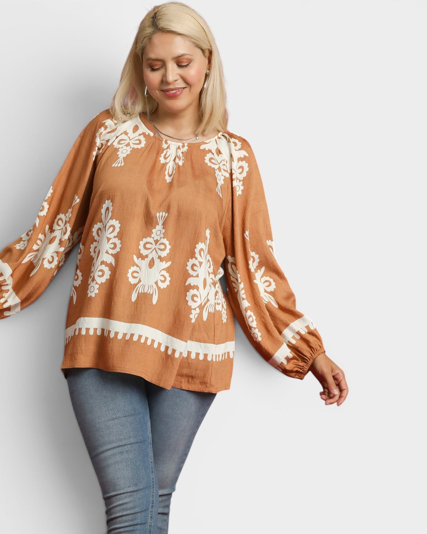 Woman wearing a brown blouse with white embroidery on a plain background