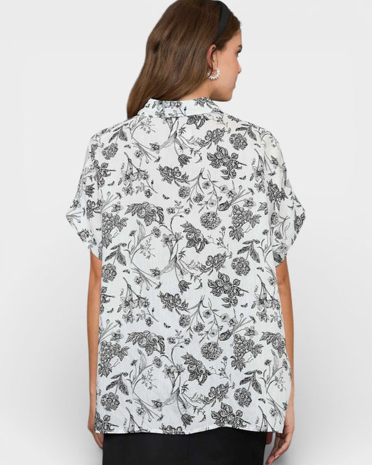 Woman wearing a white floral blouse against a plain background