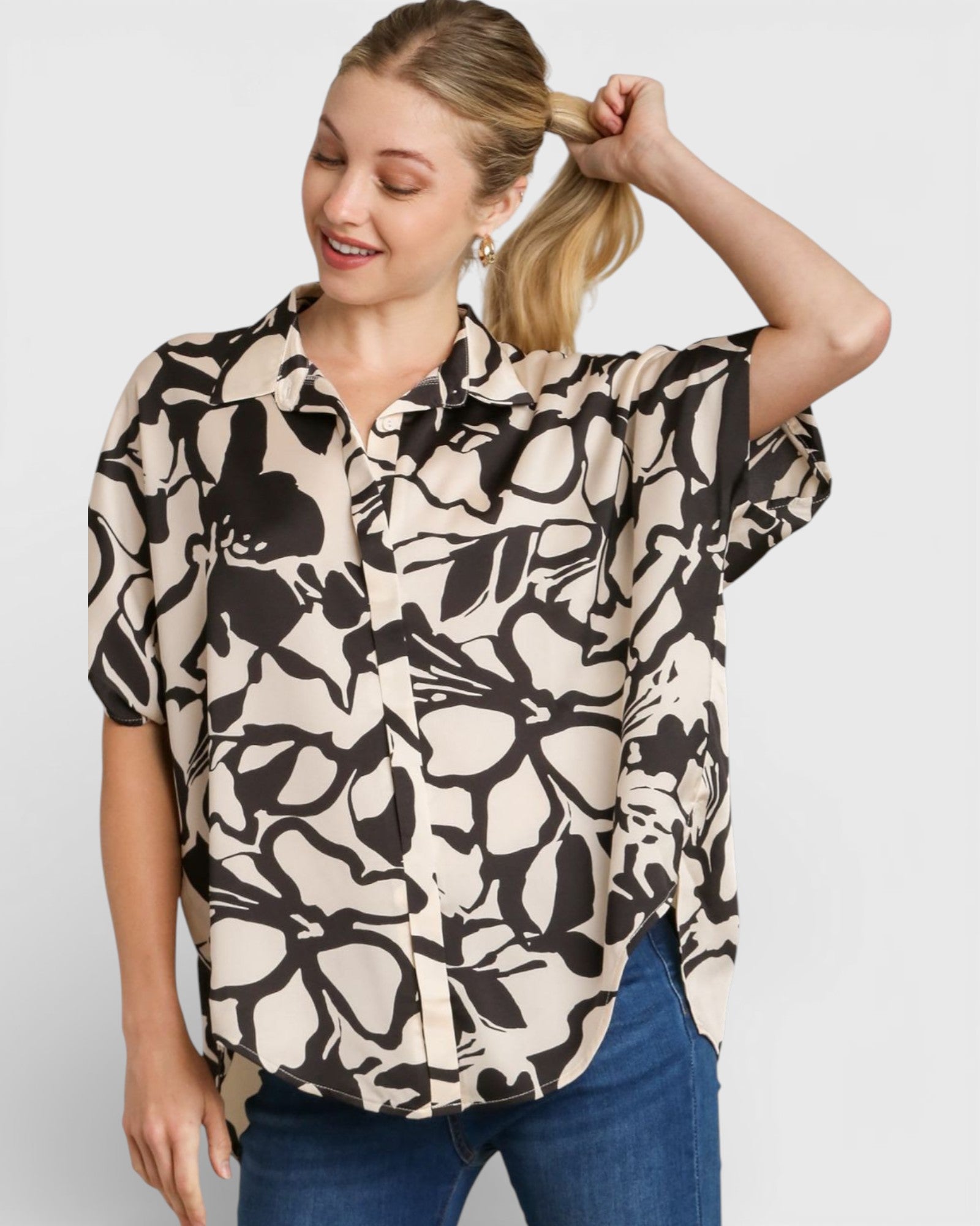Woman wearing a patterned blouse and blue jeans on a plain background