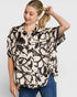 Woman wearing a patterned blouse and blue jeans on a plain background