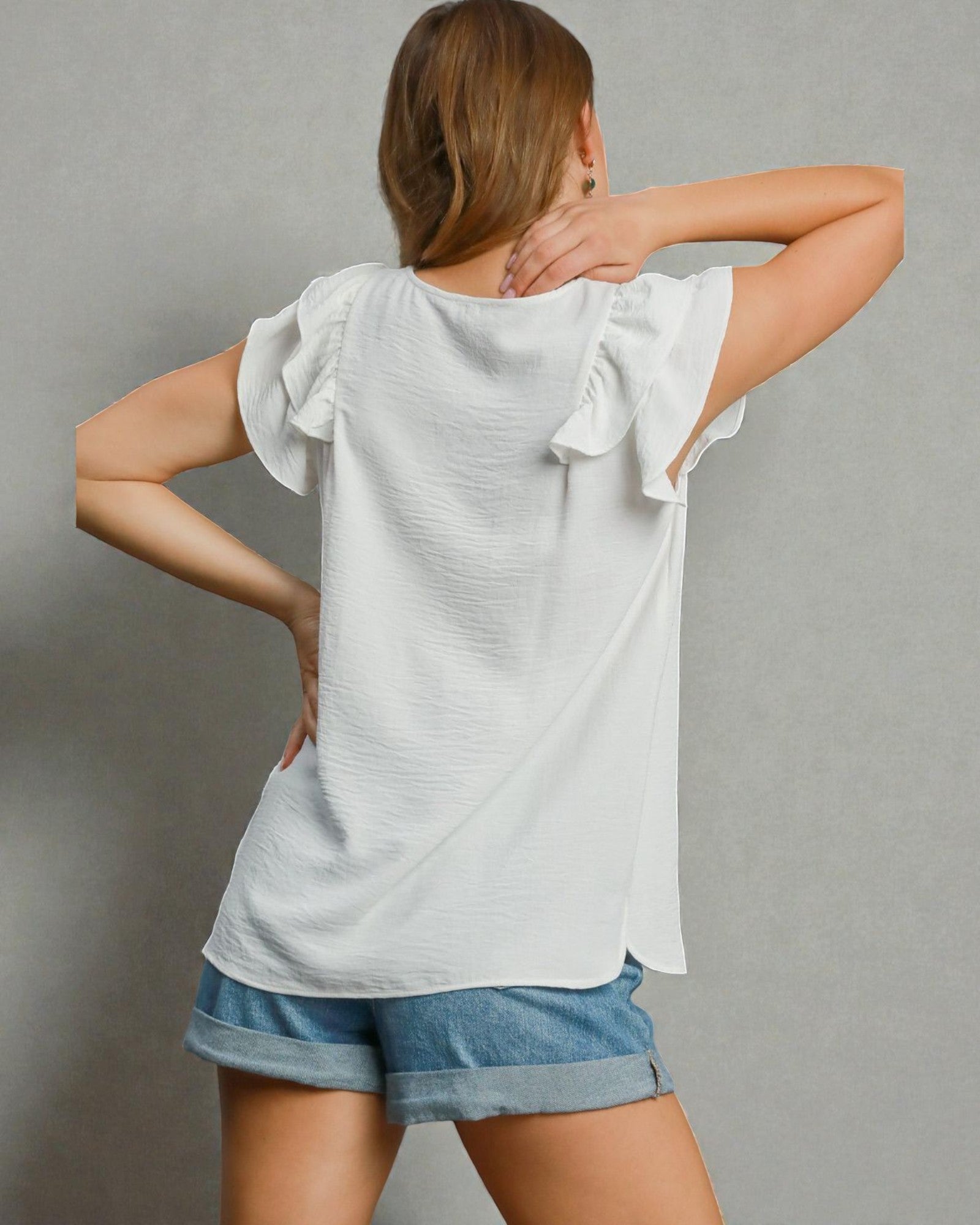 Woman wearing a white blouse with ruffled sleeves and denim shorts on a gray background
