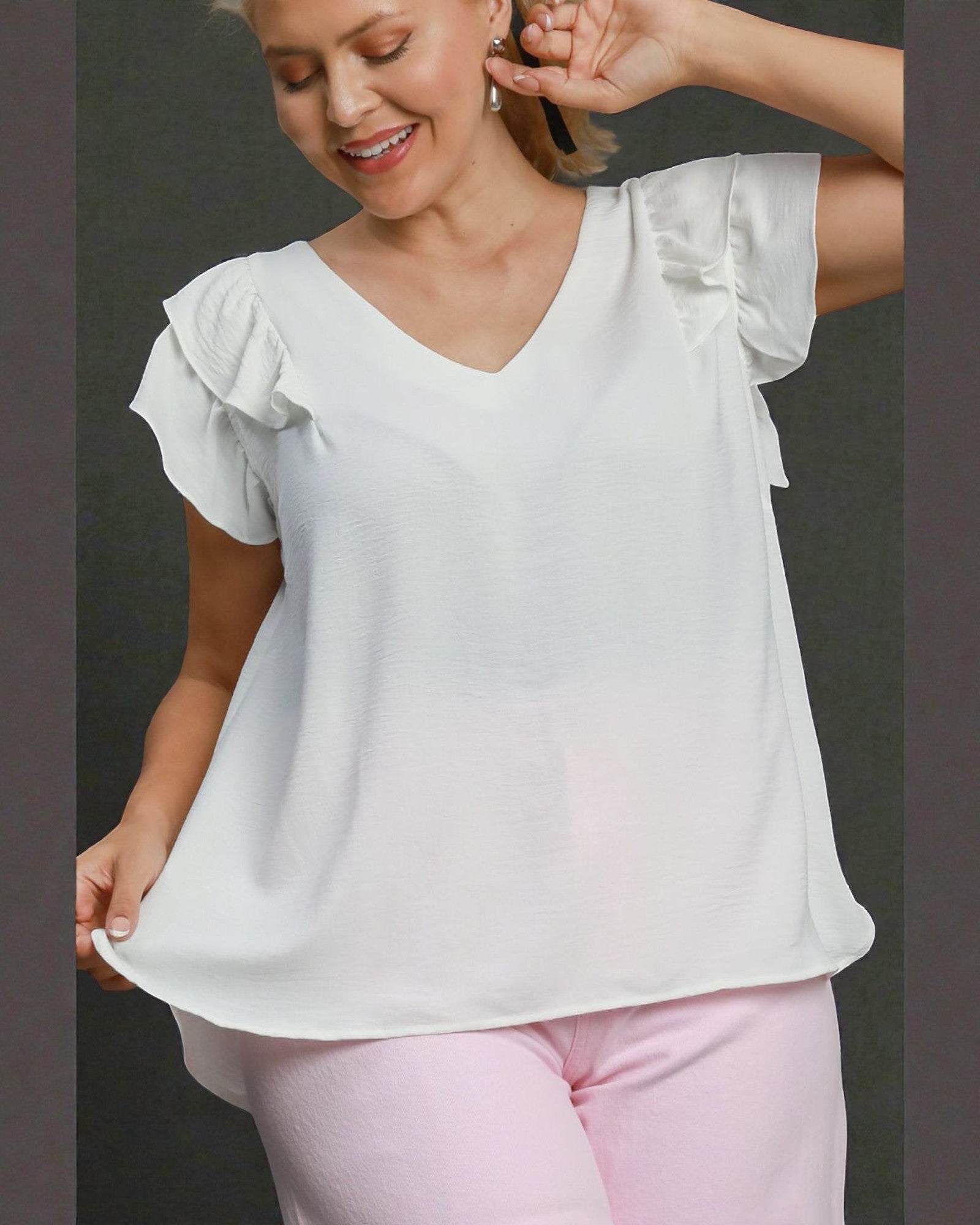 Woman wearing a white blouse with ruffled sleeves and pink pants on a dark background
