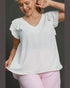 Woman wearing a white blouse with ruffled sleeves and pink pants on a dark background