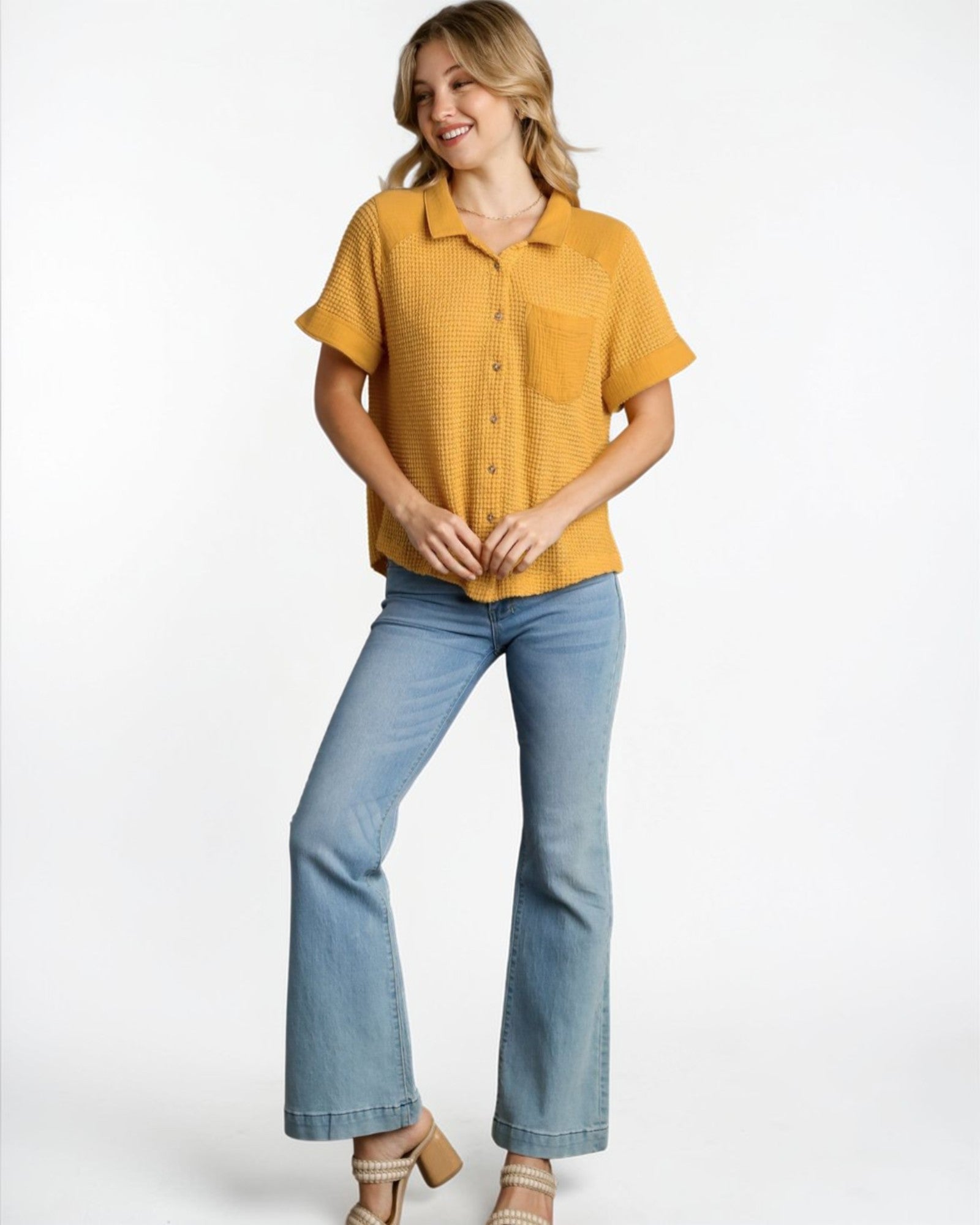 Woman wearing a mustard yellow short-sleeve shirt and light blue jeans on a white background