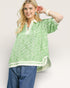 Woman wearing a green patterned top and blue jeans on a plain background