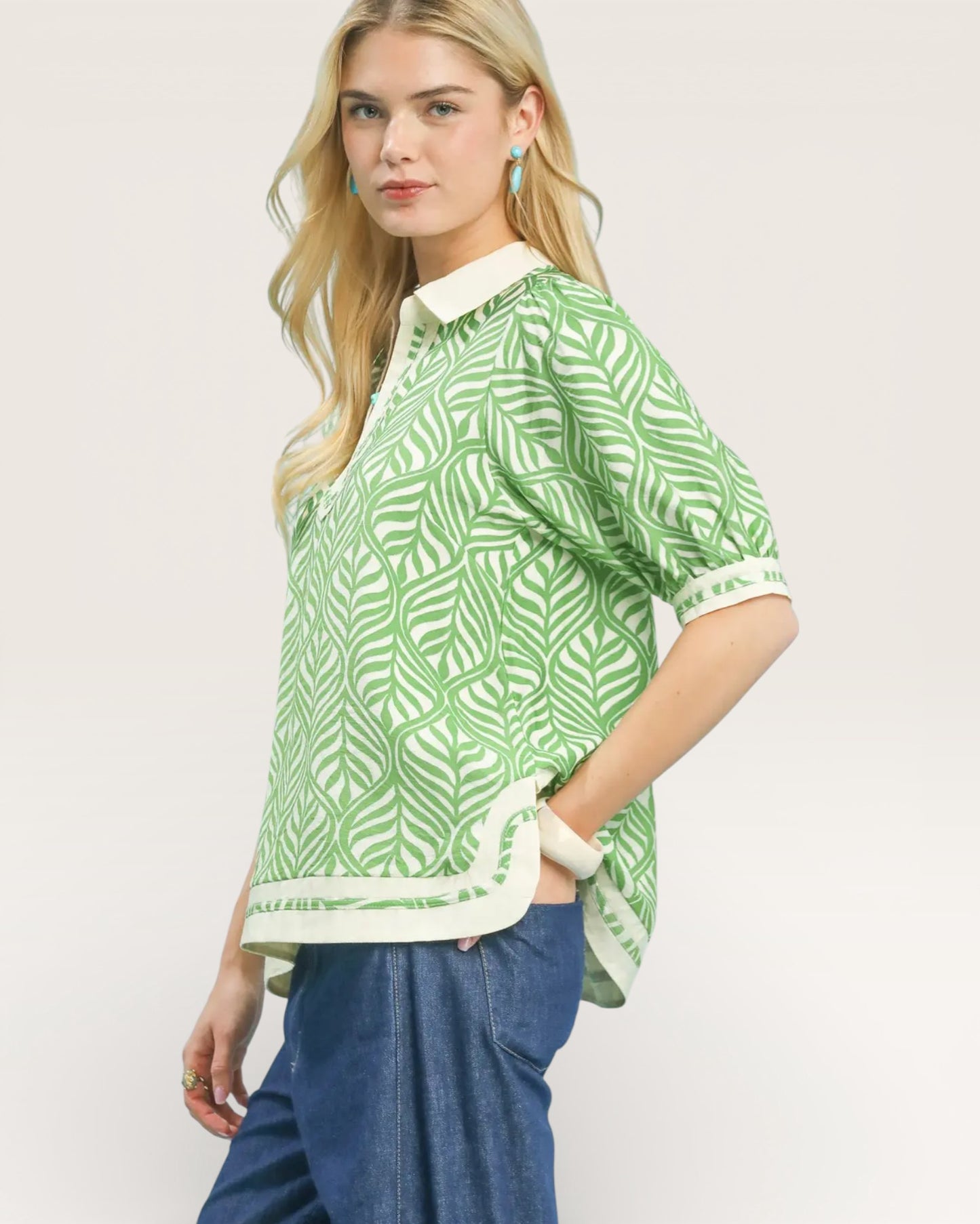 Woman wearing a green patterned shirt with a white collar on a plain background