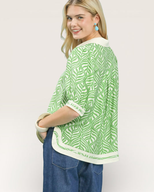 Woman wearing a green and white patterned top with blue jeans on a plain background