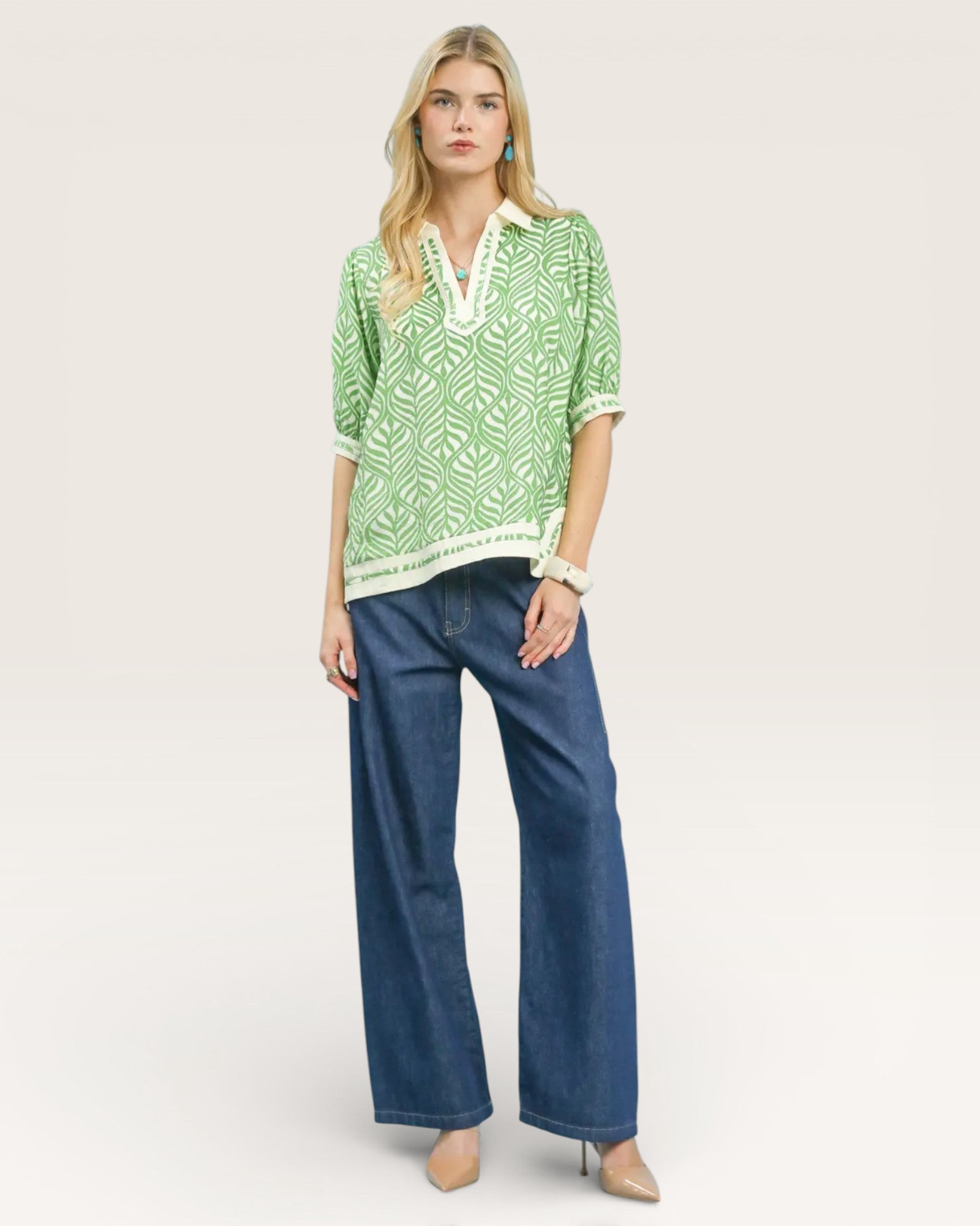 Woman wearing a green patterned top and blue jeans on a white background