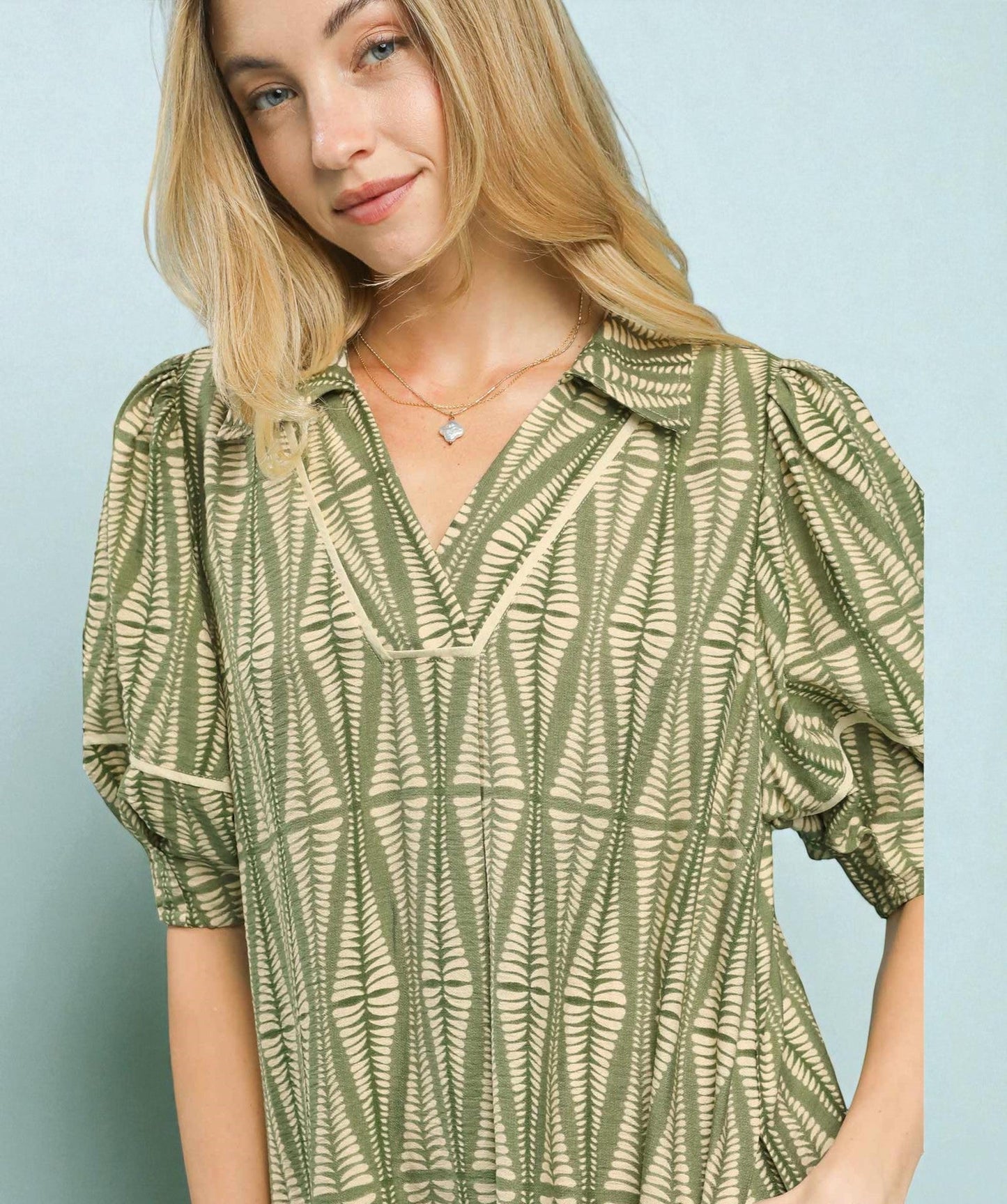 Woman wearing a green patterned blouse against a light blue background