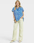 Woman wearing a blue patterned top and white pants on a white background
