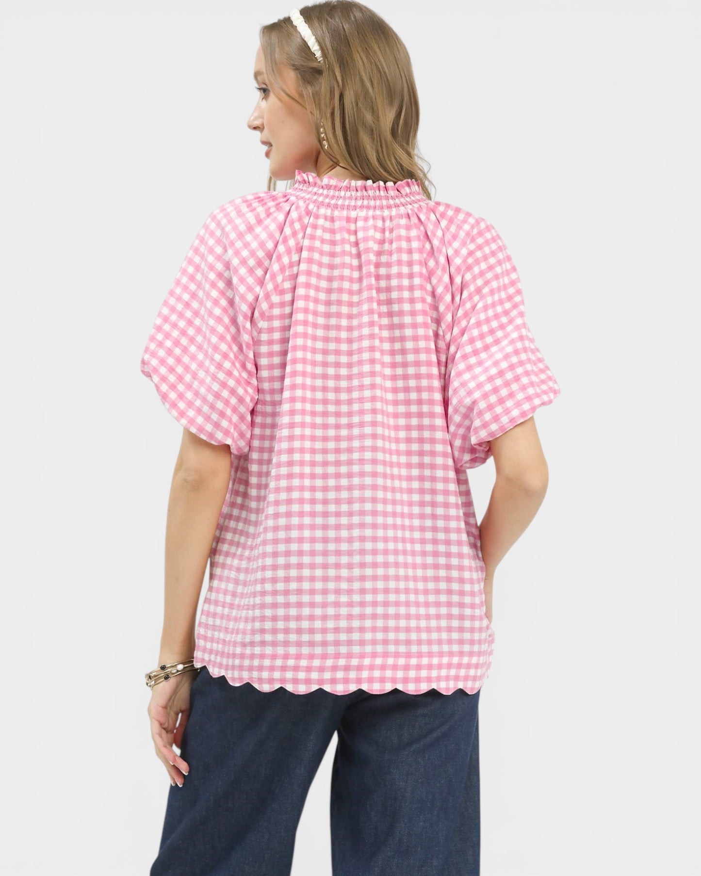 Woman wearing a pink gingham blouse and dark pants on a white background