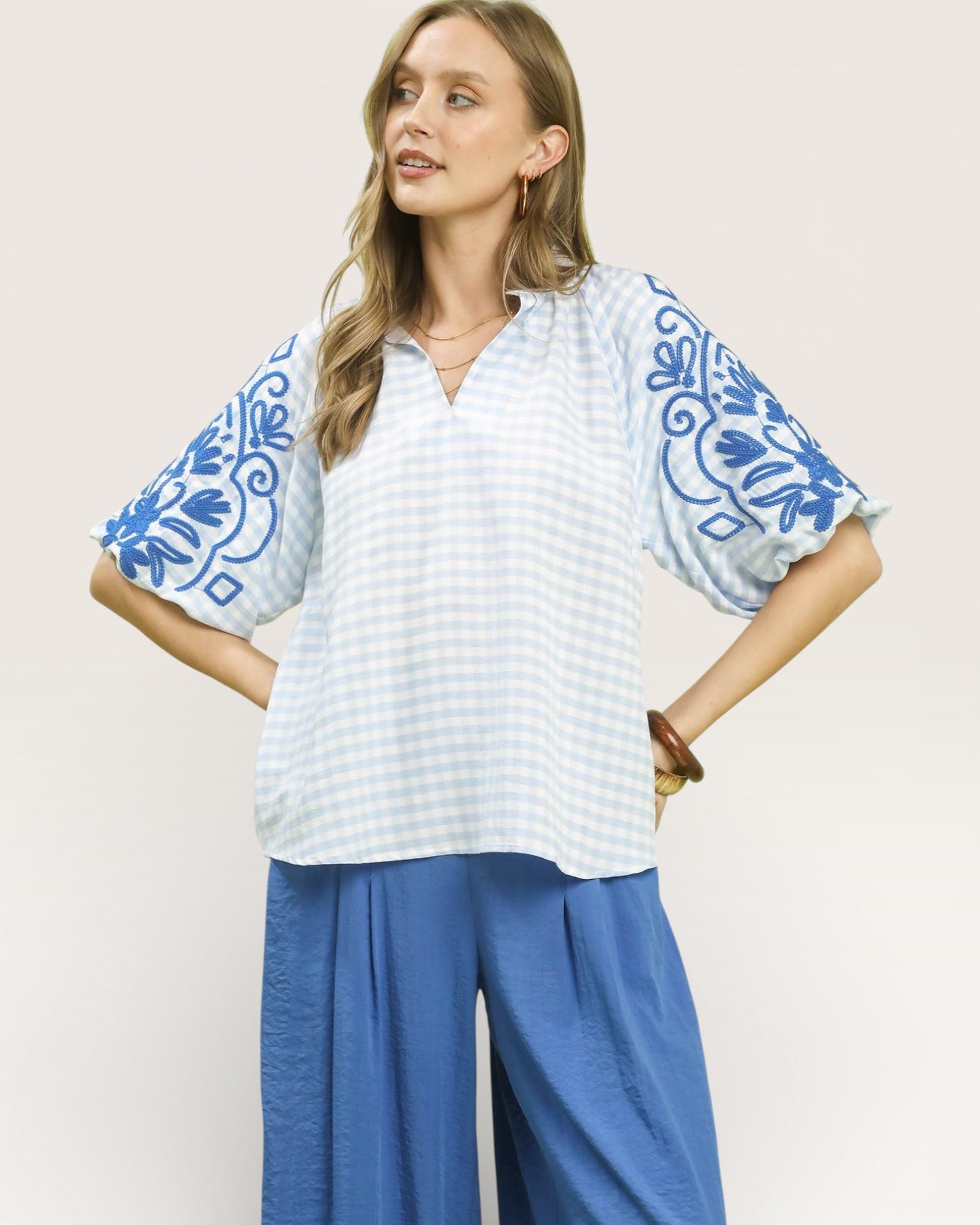 Woman wearing a white blouse with blue floral patterns and blue pants on a light background