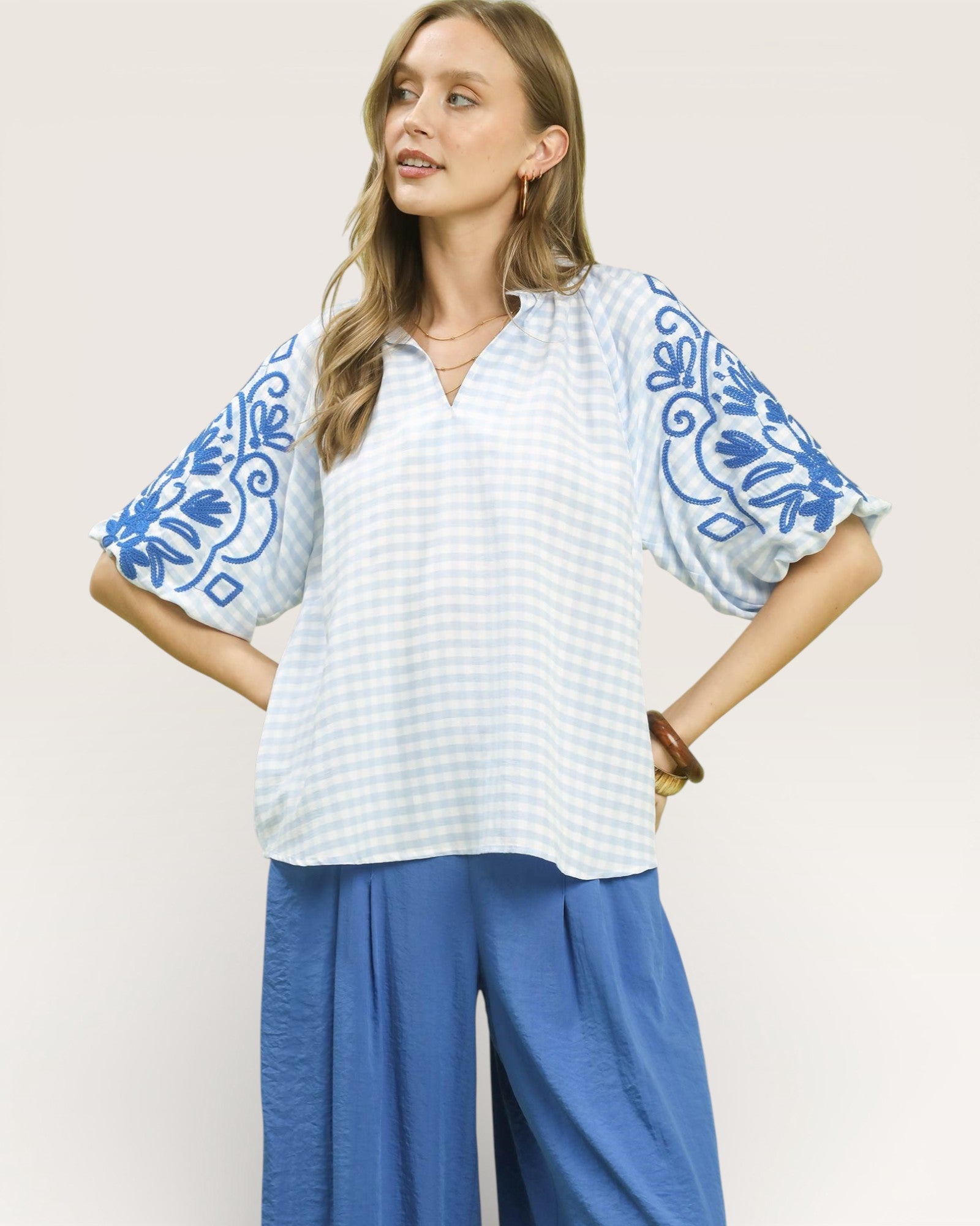 Woman wearing a white blouse with blue floral patterns and blue pants on a light background