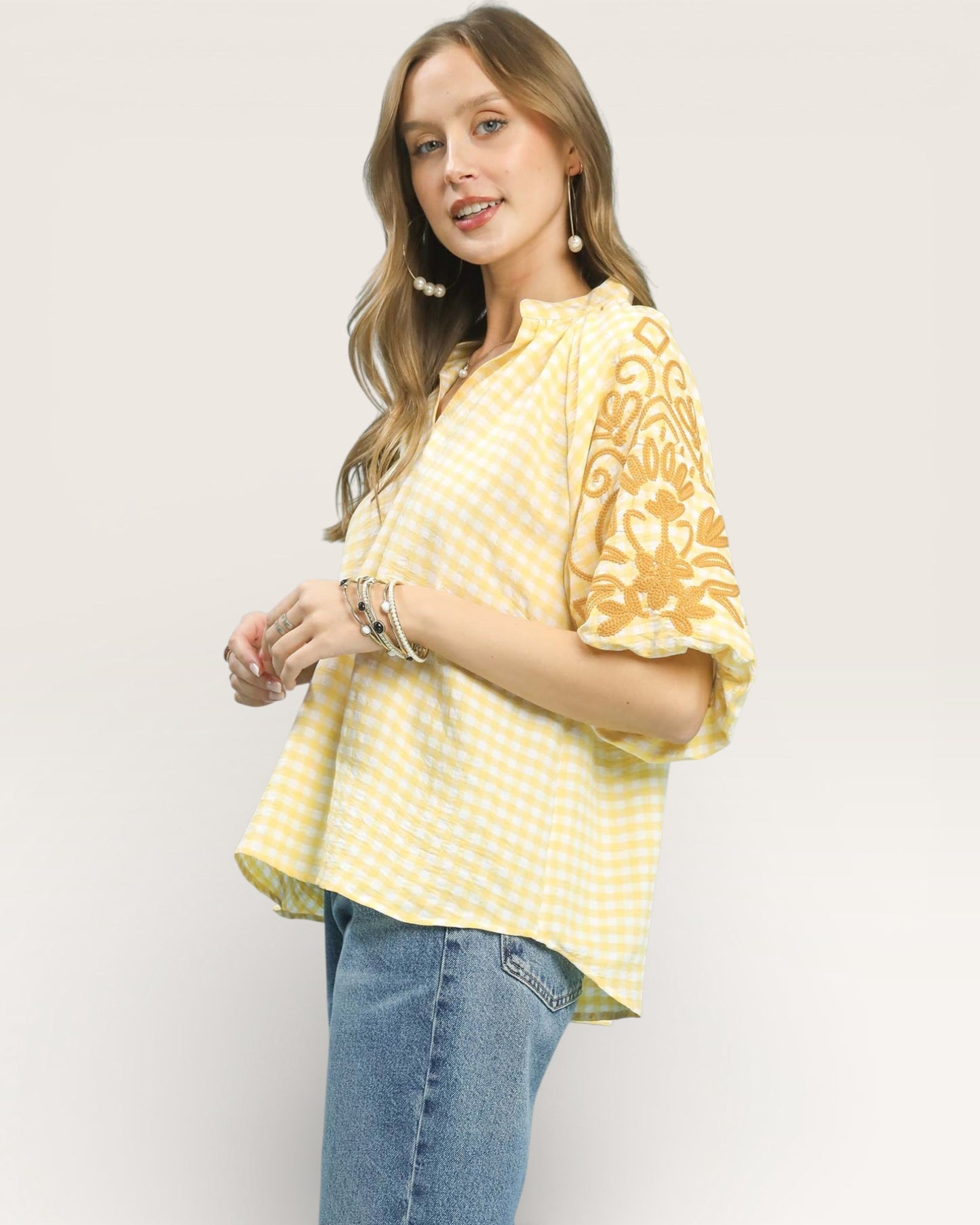 Woman wearing a yellow patterned top and blue jeans on a white background