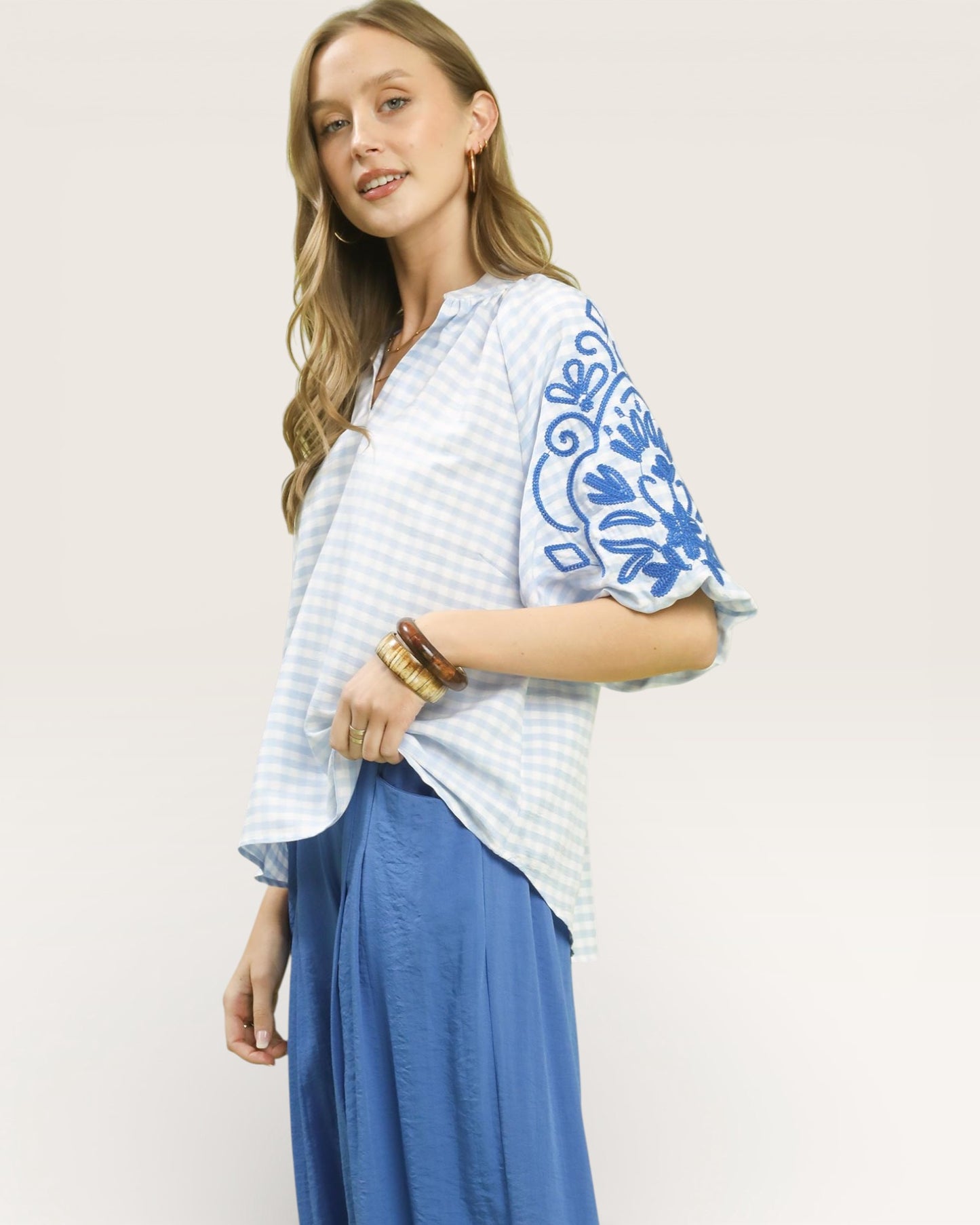 Woman wearing a light blue top with floral embroidery and blue pants on a white background