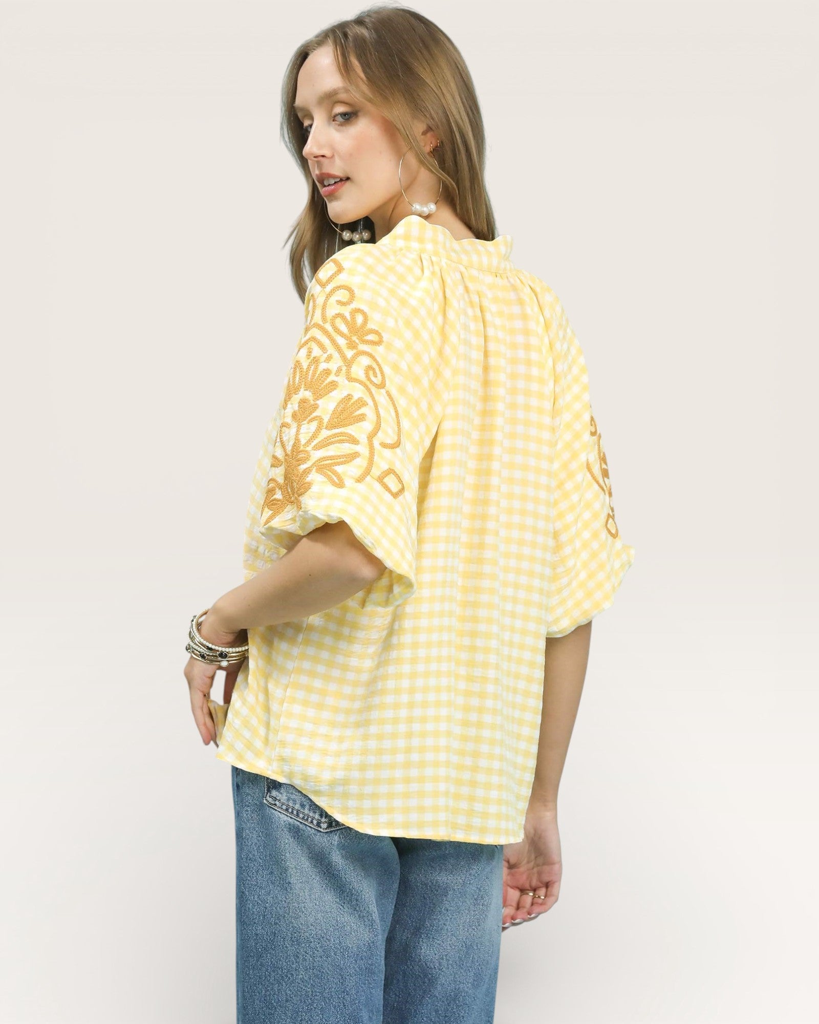 Woman wearing a yellow patterned blouse and blue jeans on a white background