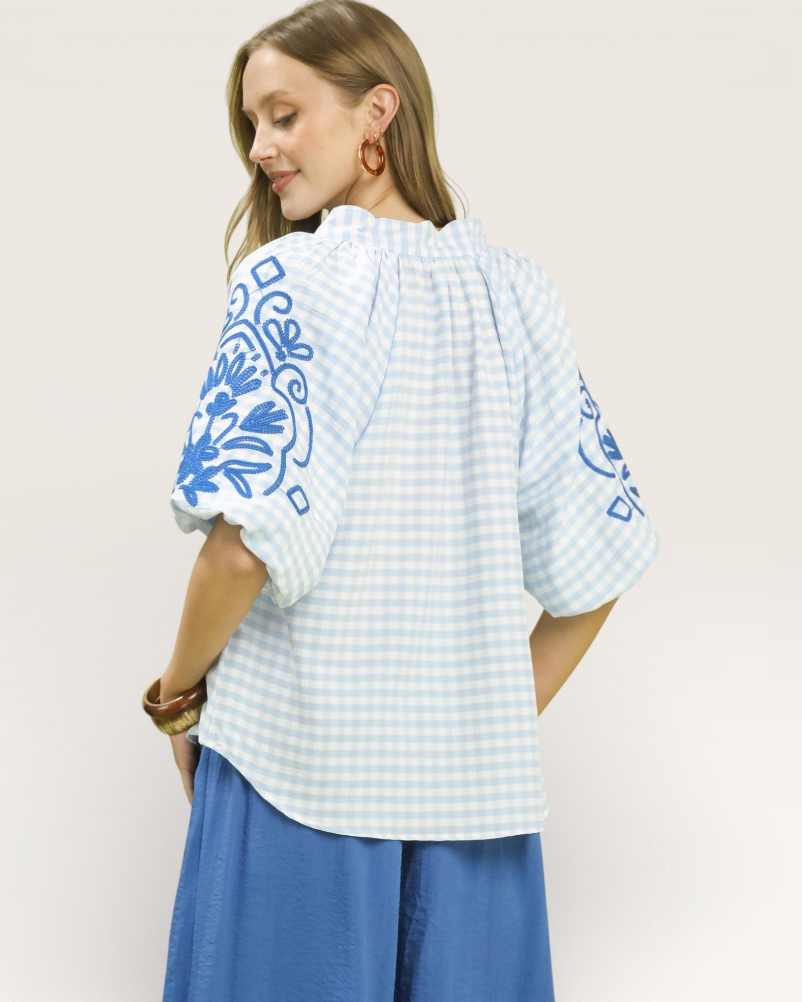 Woman wearing a white blouse with blue patterns on a plain background