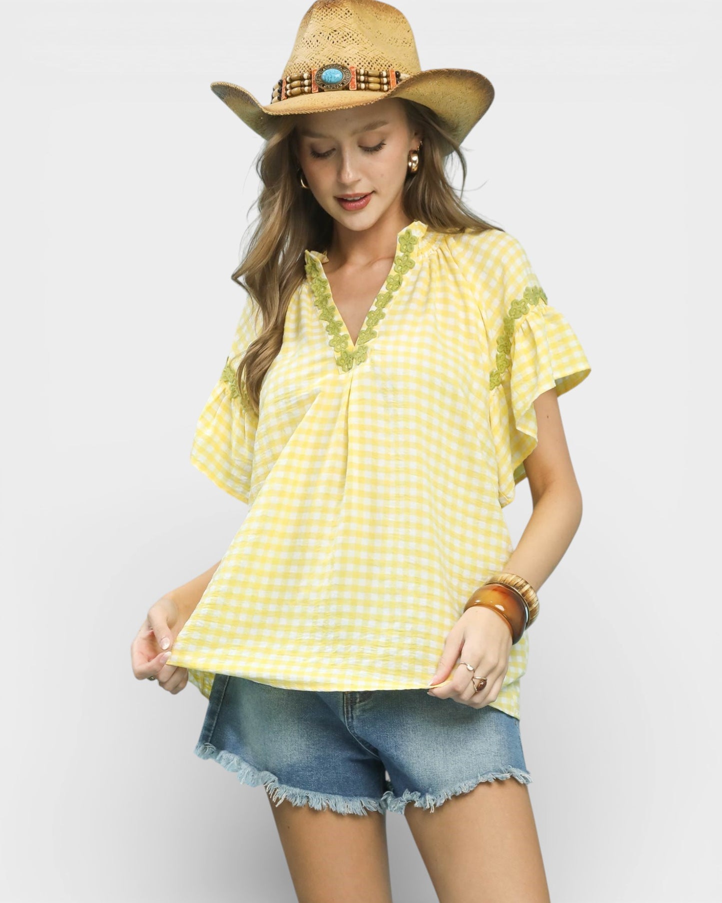 Woman wearing a yellow checkered top and denim shorts with a straw hat on a white background