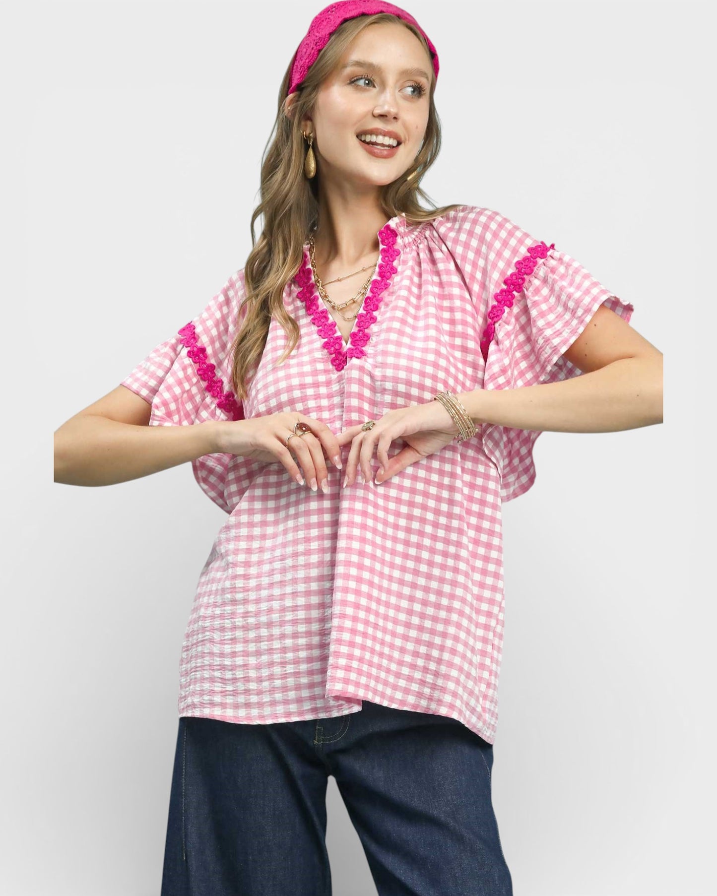 Woman wearing a pink and white checkered top with decorative trim on a plain background