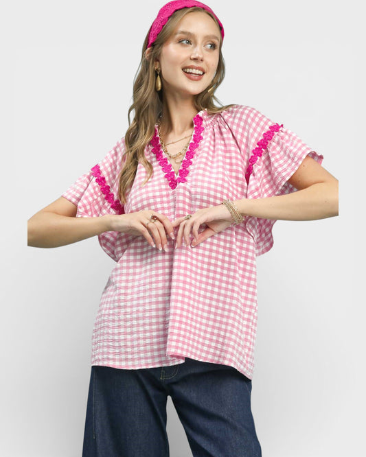 Woman wearing a pink and white checkered top with decorative trim on a plain background