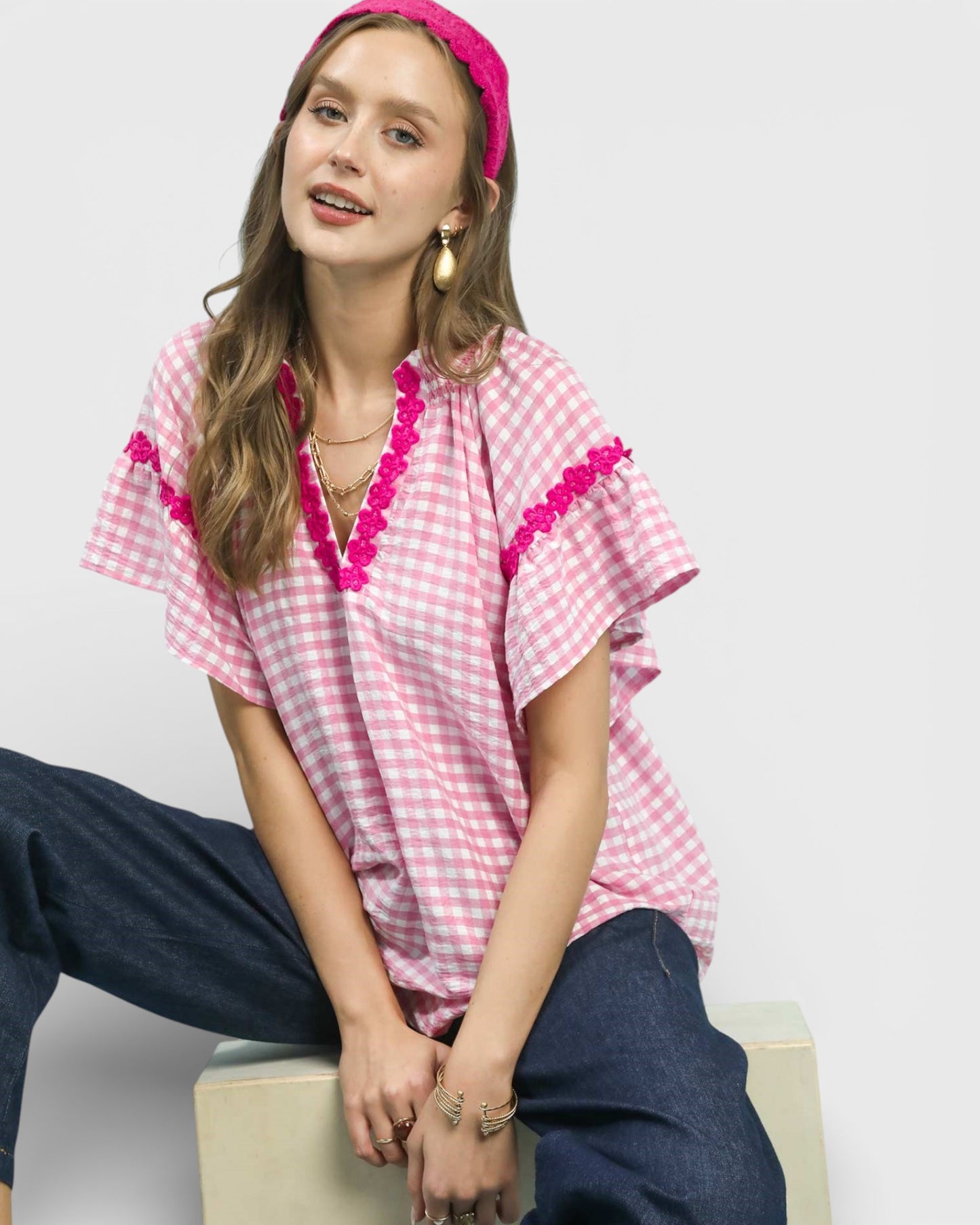 Woman wearing a pink checkered top with ruffled details and a pink headband against a white background