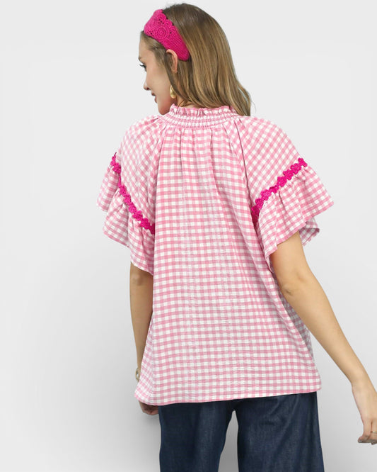 Woman wearing a pink checkered top with lace trim on a white background