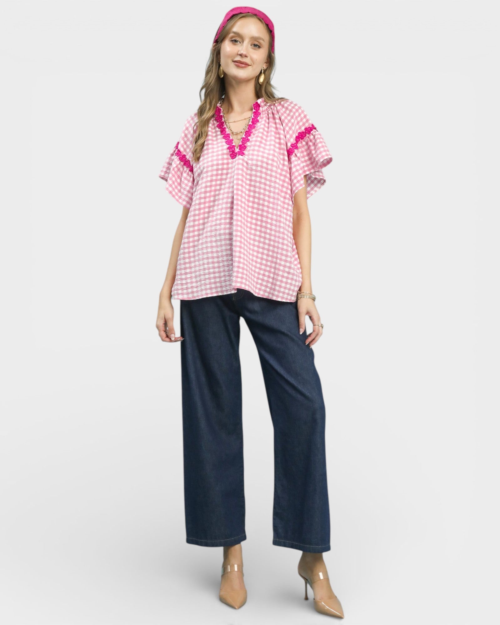 Woman wearing a pink checkered top with red trim and dark blue pants on a white background