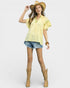 Woman wearing a yellow top, denim shorts, and cowboy boots on a white background