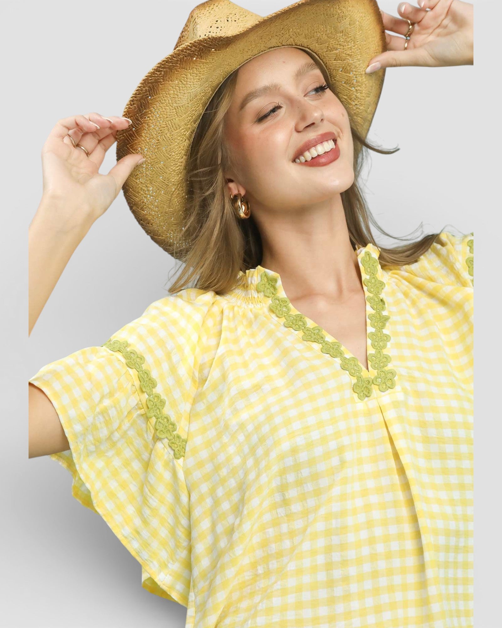 Woman wearing a yellow and white patterned dress with a straw hat on a light gray background