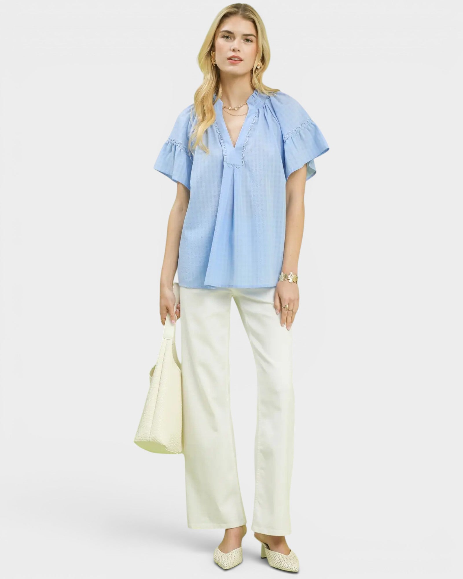 Woman wearing a light blue blouse and white pants on a white background