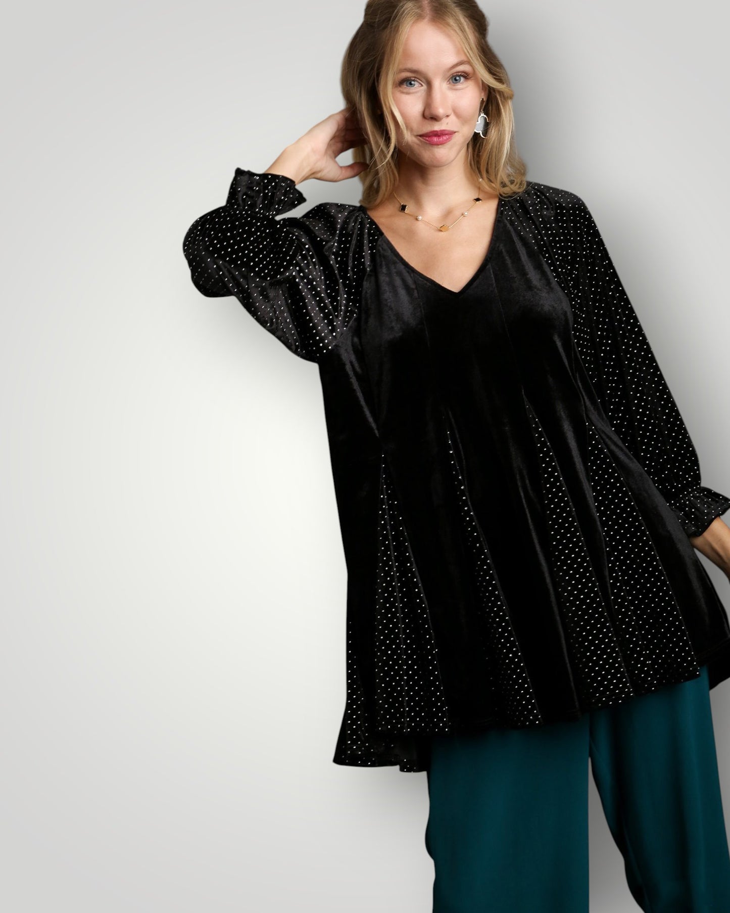 Woman wearing a black polka dot blouse and teal pants against a white background