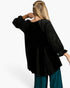 A woman shown from the back wearing a black velvet top with sheer polka-dot sleeves and teal wide-leg pants, against a plain white studio background.