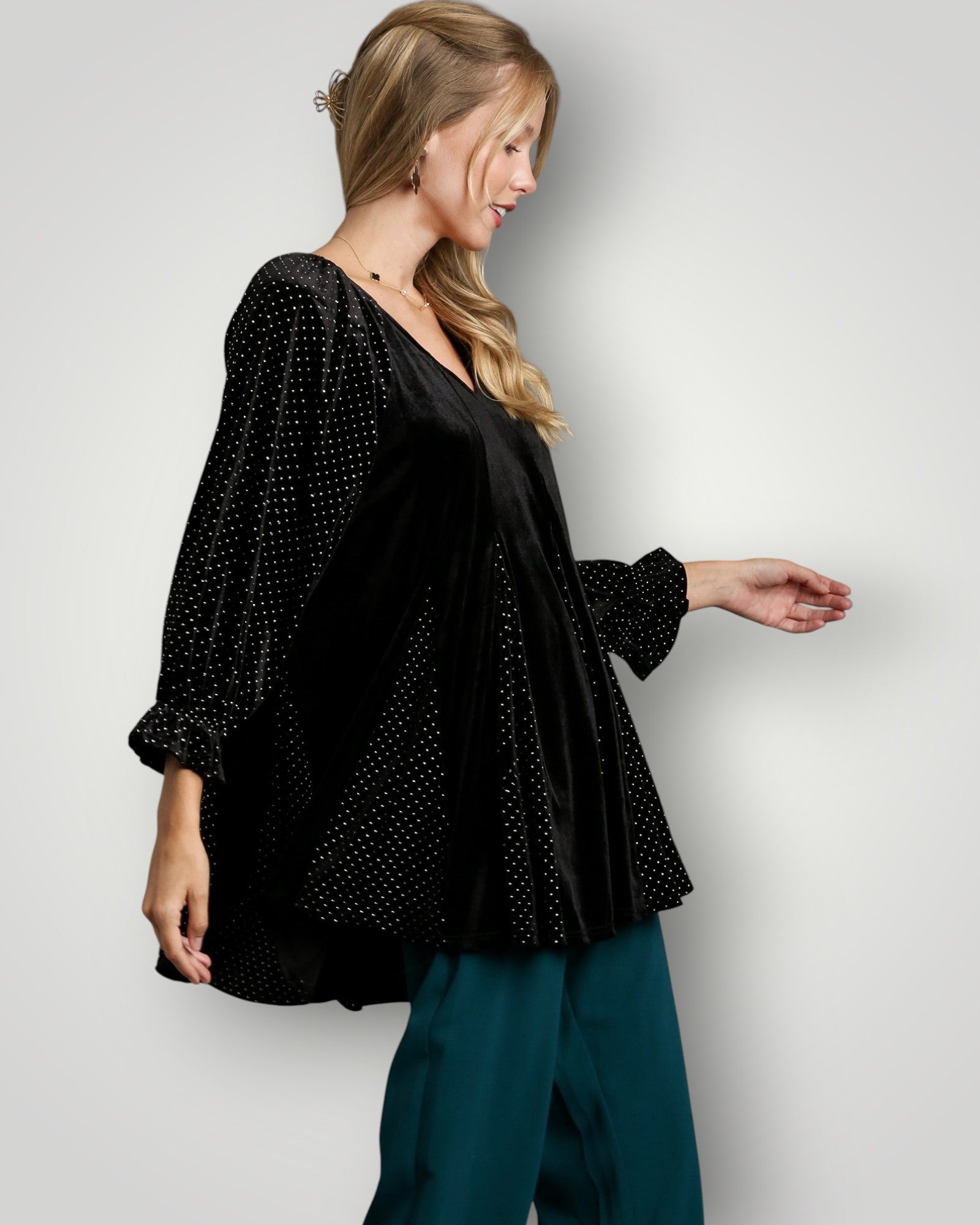 Woman wearing a black polka dot blouse and teal pants against a white background