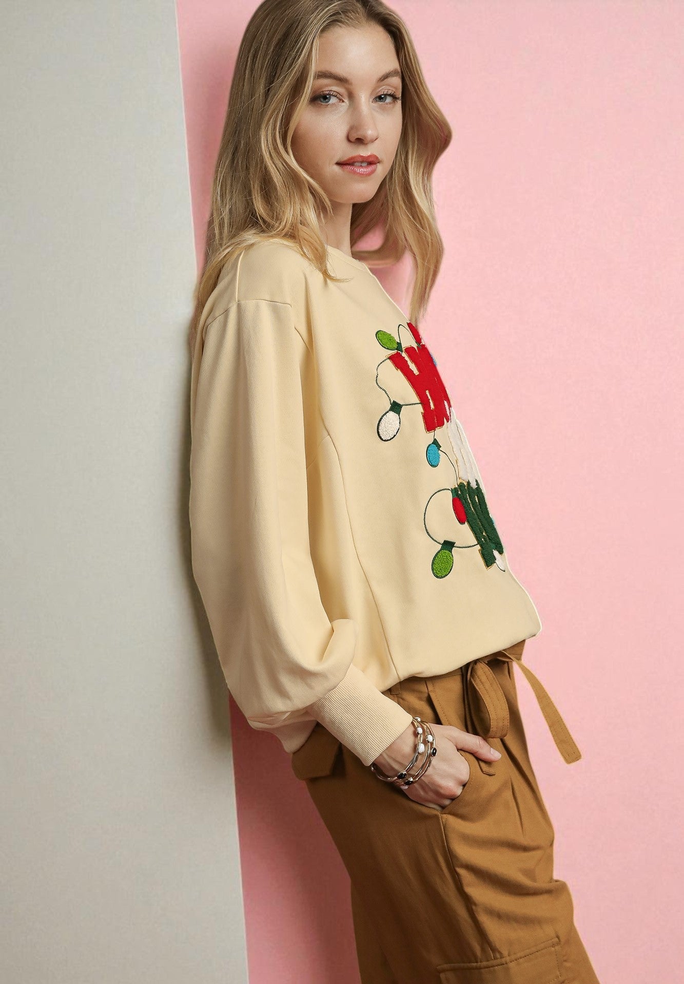 Woman wearing a beige sweatshirt with colorful graphics against a pink wall.