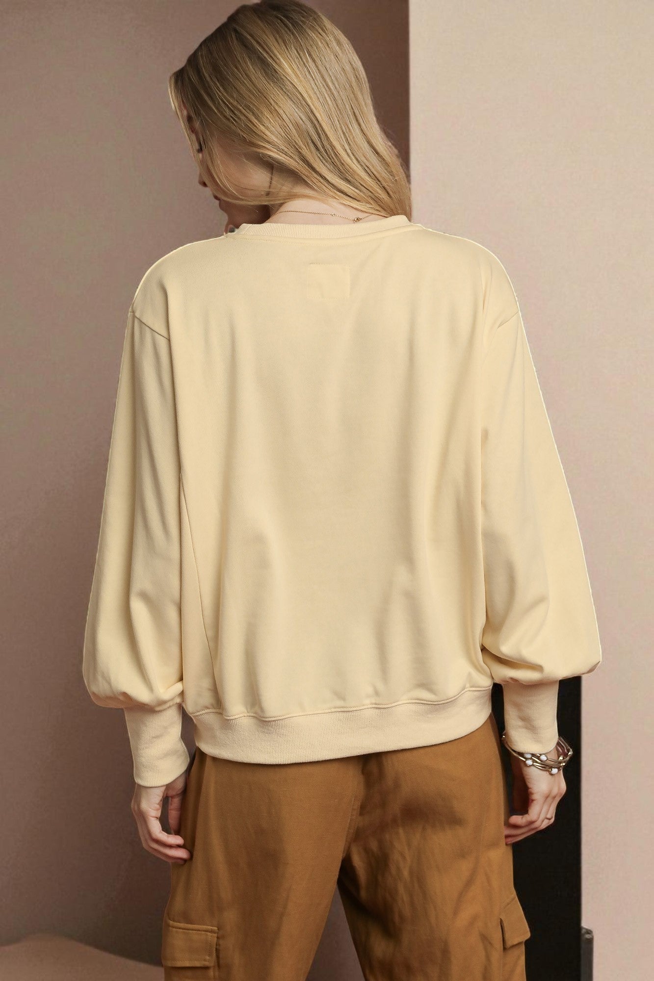 Person wearing a beige sweater and brown pants against a plain background