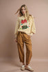 Woman wearing a beige sweater with colorful text and brown pants on a beige background