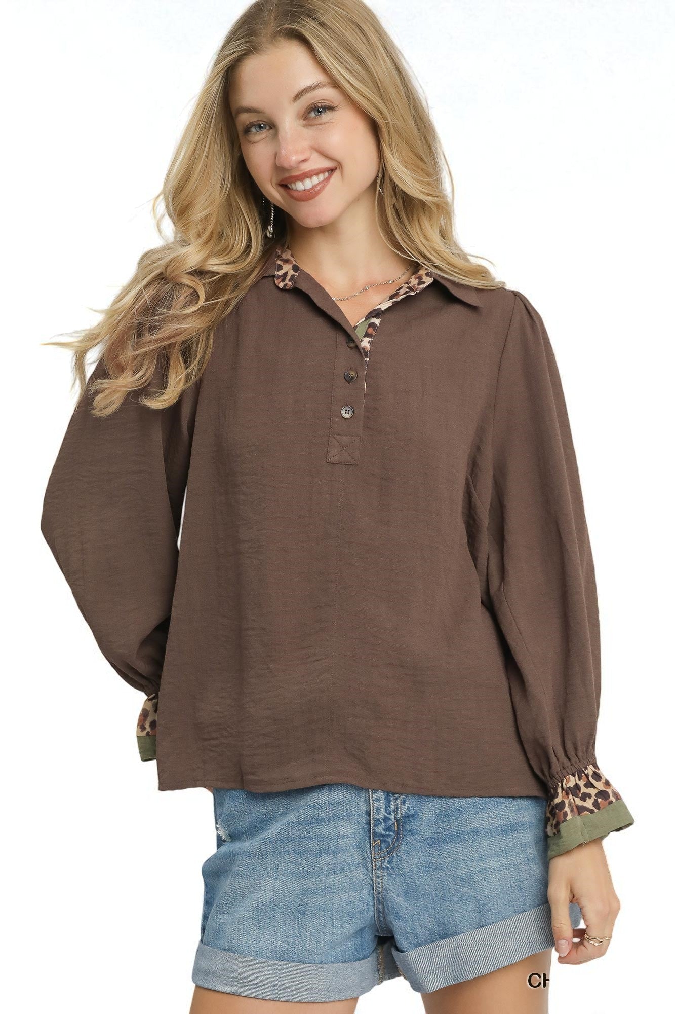 Woman wearing a brown long-sleeve shirt with patterned cuffs and collar, paired with denim shorts on a white background.