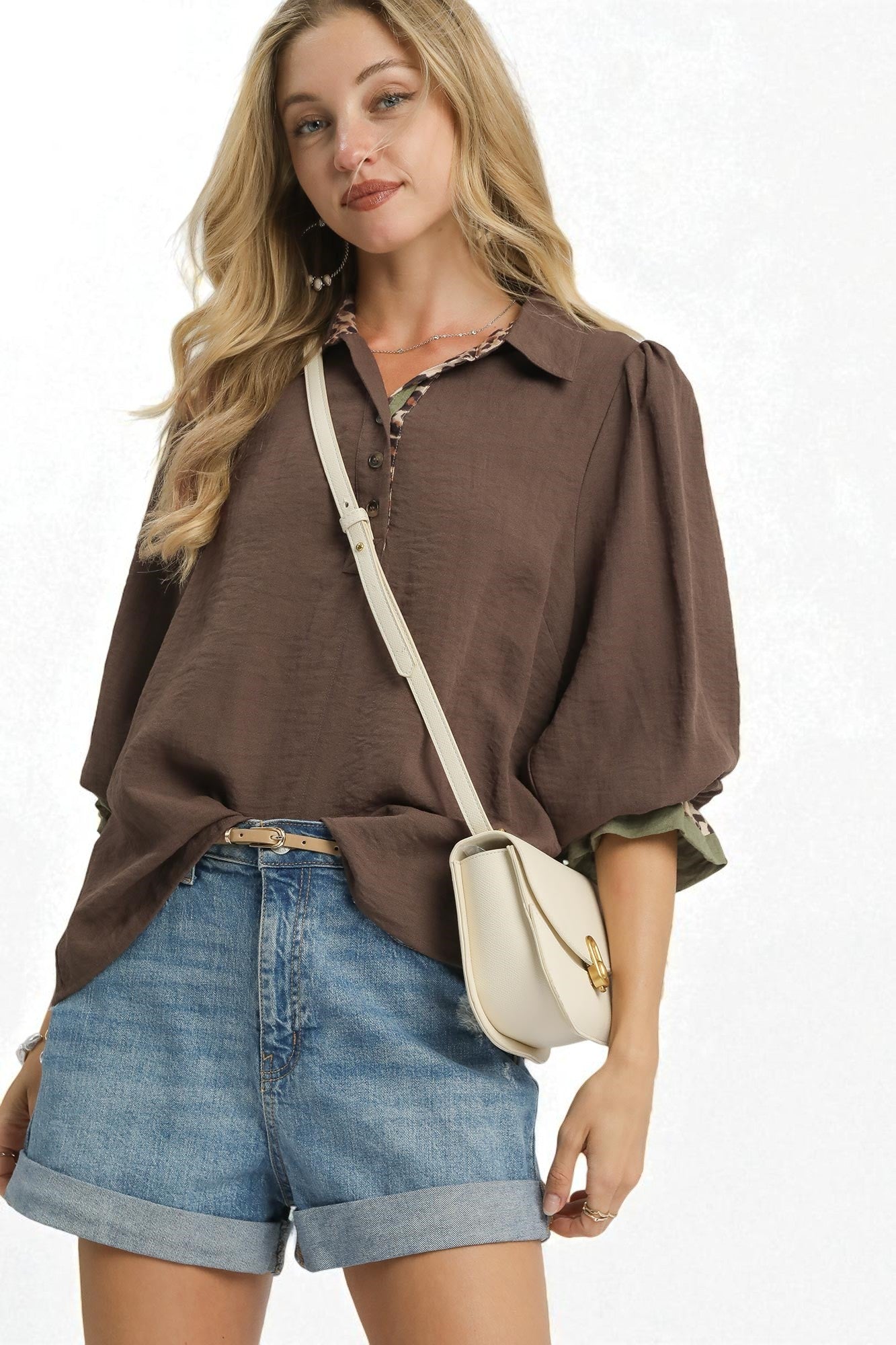 Woman wearing a brown shirt and blue shorts with a beige crossbody bag on a white background